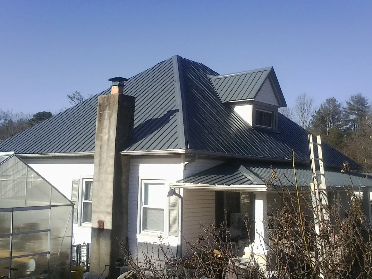 Dark blue standing seam metal roof on a white farmhouse with dormer — Slate & Tile Roof Repair by Roofing Brothers in Dime Box