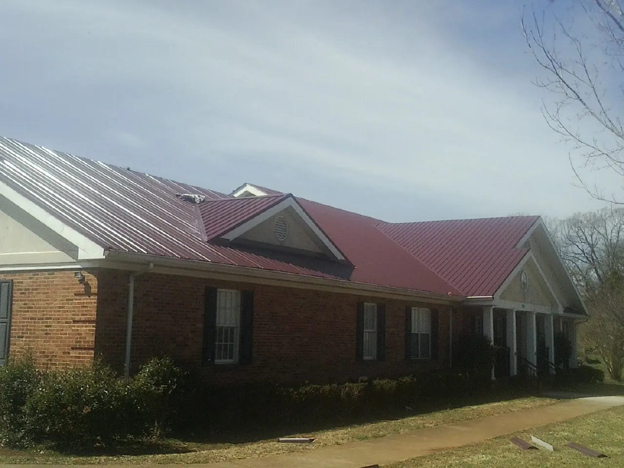 Red metal roof with gabled entries on a long brick building, from a Hail Damage Roof Repair job in Dime Box