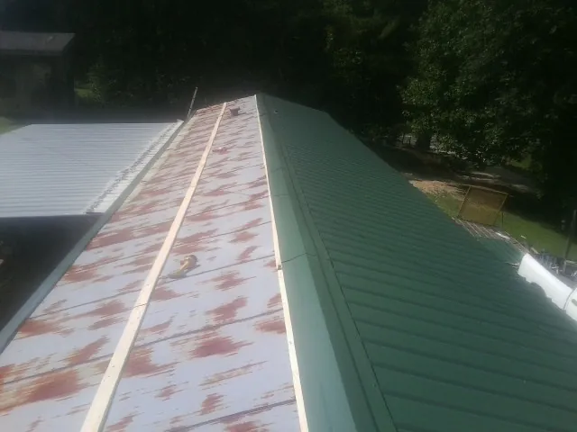 Old rusted panels beside newly installed green metal roofing — Wind Damage Roof Repair by Roofing Brothers in Dime Box