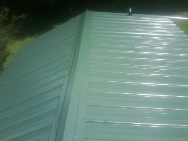 New green metal panels meeting at the ridge of a roof — Flat Roof Repair work by our crew in Dime Box