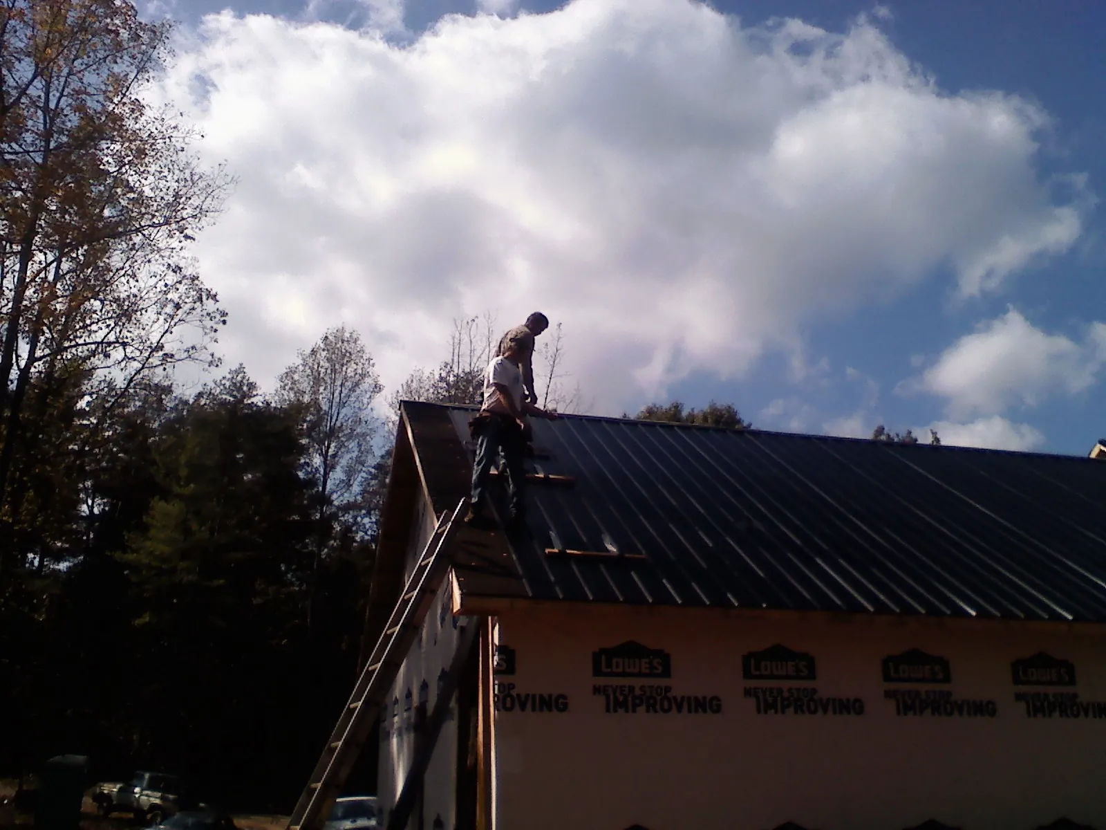 Roofer fastening dark metal panels high against a cloudy sky, from a Roof Inspection job in Dime Box