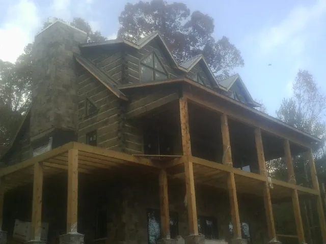 Stone chimney and dormers on a large log home with a timber porch in Dime Box