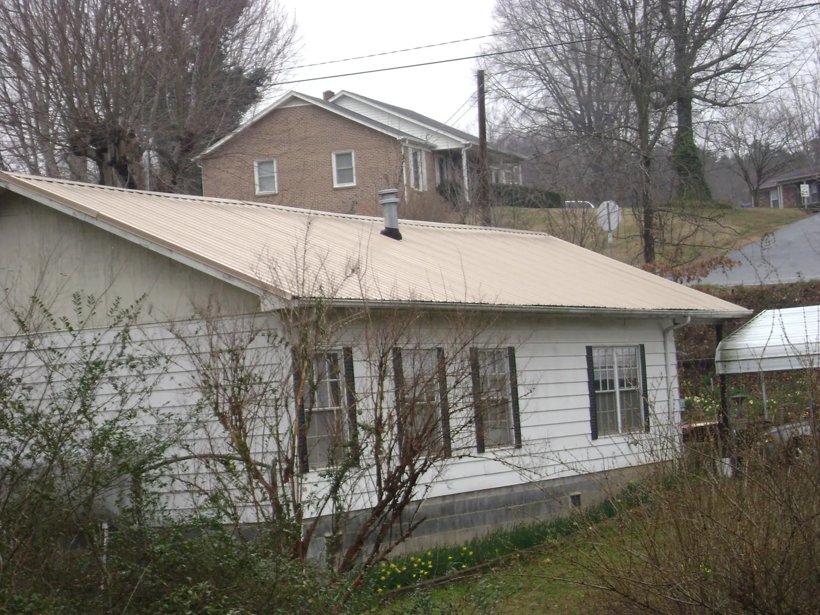 Tan metal roof on a white sided house set into a hillside — Commercial Roofing by Roofing Brothers in Dime Box
