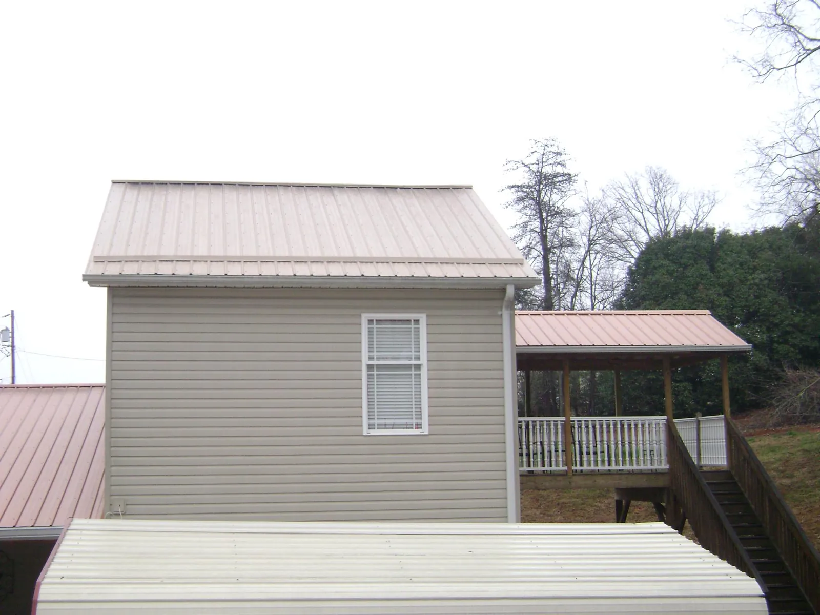 Tan metal roofs on a two story addition and attached porch, from a Roof Replacement job in Dime Box