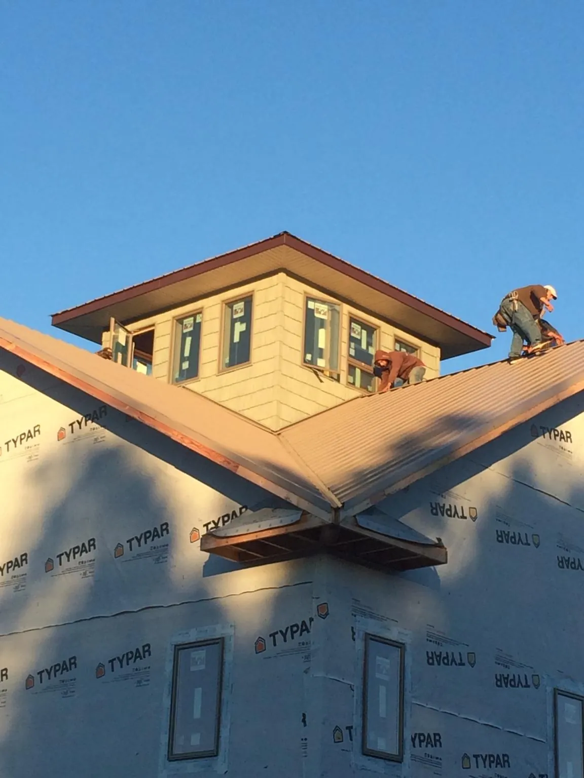 Roofers working around a rooftop cupola on a new metal roof at sunset — Roof Waterproofing in Dime Box by Roofing Brothers
